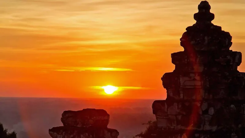 The sun setting over the plain beside a sandstone temple tower, the finale of a full-day Angkor Wat tour with sunset