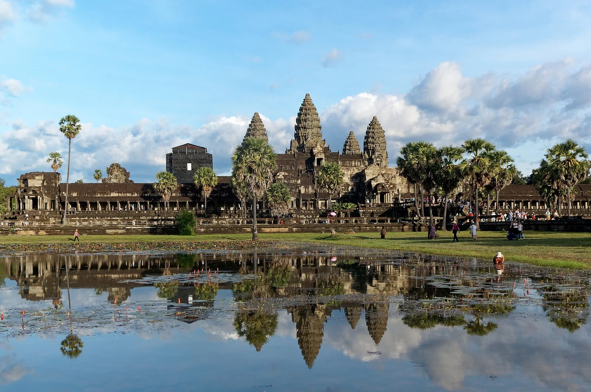 The five towers of Angkor Wat's central structure and the west-side galleries reflected in the pond under a blue daytime sky, seen on Angkor Wat tours from Siem Reap